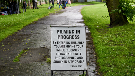 Photo of a 'Filming in Progress' sign in a park.