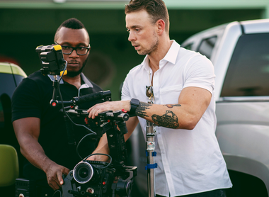 Photo of two people on location stood holding a RED camera on a gimbal.