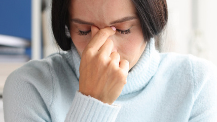 A woman is sitting with her head down, pinching the bridge of her nose with her fingers. She looks upset.