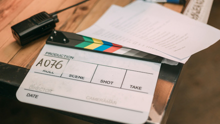 Photo of a desk with a clapper board, walkie talkie and script pages on it.