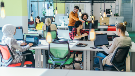 Photo image of an open plan office with colourful chairs and a diverse group of employees spread across the desks.