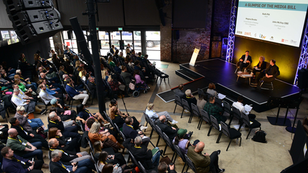 Overhead shot of a conference audience facing a stage on the right of the image.