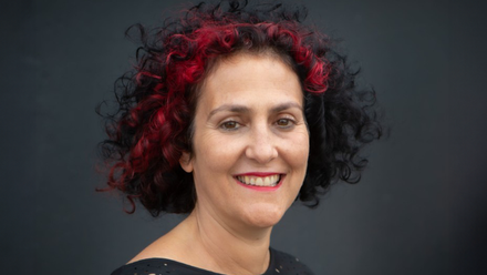 Headshot: a woman with short curly black hair with red highlights wearing a black top.