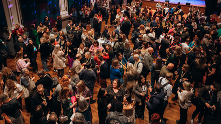 Photo taken overhead showing a large hall full of people networking over drinks.