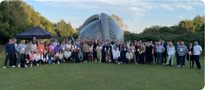 Group photo of attendees of Content Without Borders 2024 in a field with blue skies overhead, after completing The Crystal Challenge.