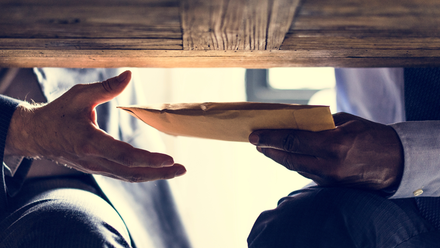 Photo close up of an unmarked envelope being passed between hands under a table.