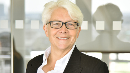 Headshot: Sara Geater, an older woman with short white hair wearing black glasses, a black jacket and white shirt.