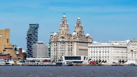 Photo of the Liverpool waterfront showing the Liver building and a mix of old and new buildings beside it on a clear, bright day.