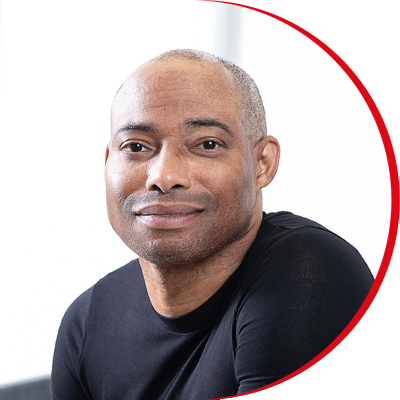 Headshot: Robert Ashton, a man with a shaven head wearing a black top.