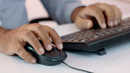 Close up of a man's hands on a black computer keyboard and mouse.