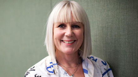 Photo of Jo Street, a woman with a straight blond bobbed hair and fringe, wearing a bright, colourful patterned top.