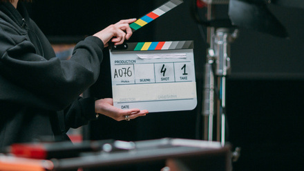 Photo taken on set, a clapper board is being held up amongst bits of equipment in the foreground and background. The board says Shot 4 Take 1.