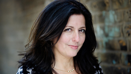 Headshot: Camilla Lewis, a woman with long, wavy black hair wearing a white and black top.