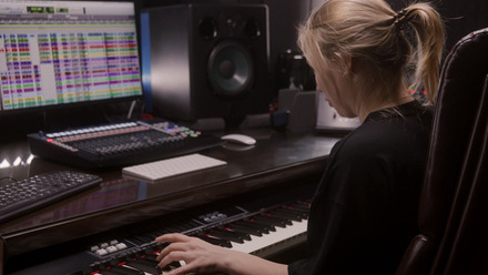 Photo taken over the shoulder of a blond haired woman wearing a black top who is sat in front of a computer screen and keyboard.