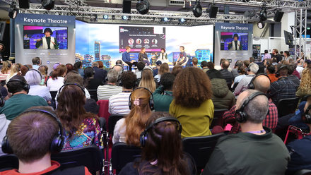 Photo of a panel event at MPTS, a large audience watches the stage which has two large screens either side.