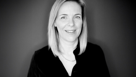 Headshot: Scarlett Ewens, a woman with long blond hair wearing a black shirt and chain necklace.