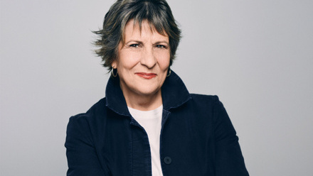 Headshot: Sara Kozak, an older woman with short dark hair wearing a white top with a navy blue jacket with the collar up.