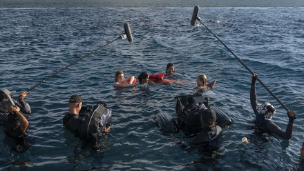 Production image from Dan Films: four young women are floating in the sea, a production crew dressed in wetsuits are filming them.