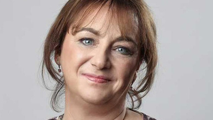 Headshot: Jane Rogerson, a woman with long brown hair tied back, wearing a brown on white top and set against a grey background.