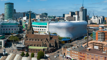 Photo of Birmingham skyline, with a mix of modern and old buildings and a blue sky overhead.