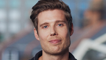 Headshot: A man with short quaffed brown hair wearing a dark shirt.