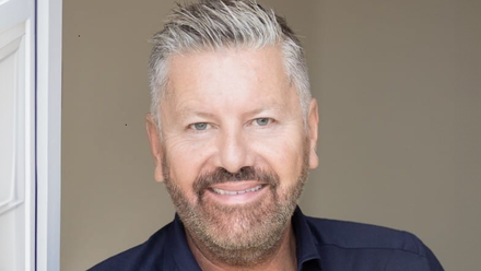 Headshot: A man with short grey/black hair and a short beard wearing a navy blue shirt.