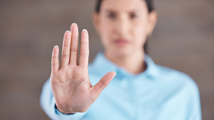 Photo of a woman holding her hand up to the camera. Her hand is in focus but her face and body behind it are out of focus.