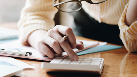 Photo close up of a woman's finger pressing a button on a calculator which is sitting on a desk.