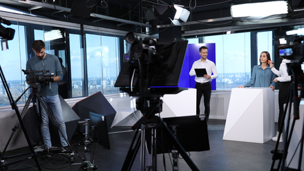 Photo of a studio set with cameras and lights set up and two presenters prepping to go live.