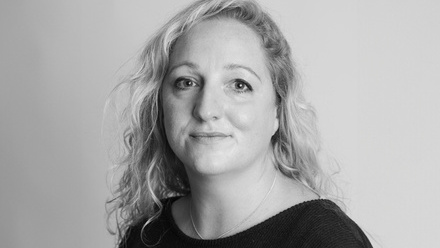 Headshot: A woman with long, curly blond hair wearing a black round-neck top.