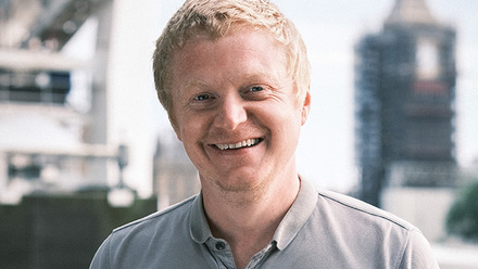 Headshot: A man with short fair hair brushed forwards wearing a grey polo t-shirt.