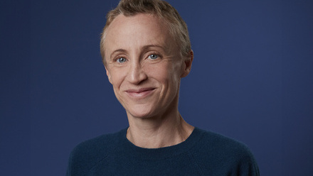 Headshot: Sam Margaritis, a woman with very short, fair hair wearing a navy blue top and smiling to camera.