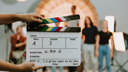 Photo of a clapper board in the foreground, with people out of focus in the background.