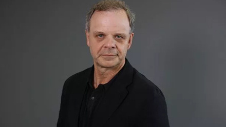 Headshot: Grant Mansfield, an older man with short fair hair wearing a black shirt.