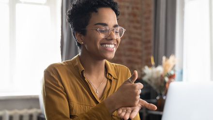 Photo of a woman sitting at a desk in front of a laptop. She is signing thumbs up.