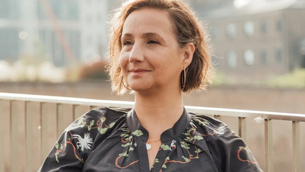 Headshot: Nicola Hill, a woman with short brown hair wearing a black patterned top.