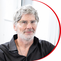 Headshot: Conrad Mewton, a man with short grey hair and beard wearing clear-framed glasses and a black shirt.