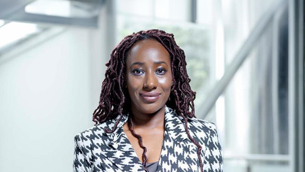 Headshot: A black woman with long dark hair, she is wearing a black and white patterned blazer.