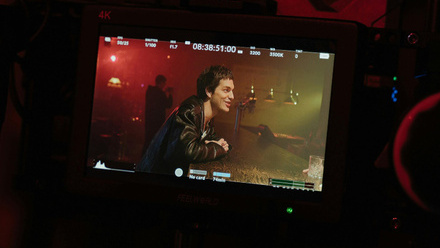 Photo close up of a monitor screen, showing a man (actor) sitting at a bar. Various levels and data are seen around the edge of the monitor.