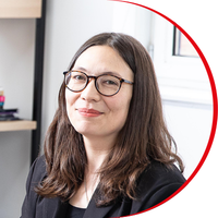 Headshot: Emily Oyama, a woman with long brown hair wearing glasses and a black jacket and top.