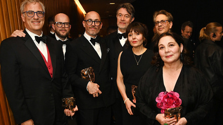 Photograph of seven members of the Conclave production team, all dressed in black tie and several holding their BAFTA Award masks.