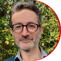 Headshot: Paul Cohen - a man with short black hair and a greying short beard wearing black-rimmed glasses and a light blue shirt.