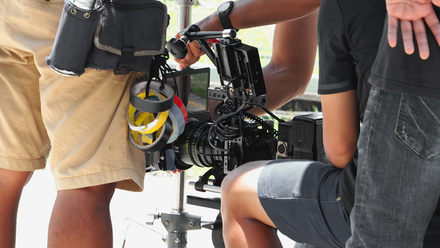 Photo close up on a camera crew, we can see the camera and some coloured tape alongside the crew members' legs.