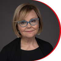 Headshot: Julie Baines, a woman with a short brown bob haircut, wearing grey-rimmed glasses and a black top and jacket.