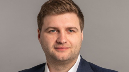 Headshot: A man with short brown hair wearing a white shirt and navy blue suit jacket.