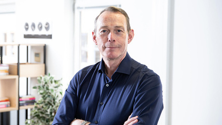 Headshot: A man with short brown hair, wearing a dark blue shirt. His arms are crossed and he is smiling at the camera.