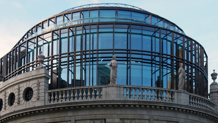 Photo of the outside of the Channel 4 HQ building in Leeds. A large, modern glass facade sits on top of a more traditional brick building with statues