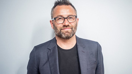 Headshot: Andrew Robertson, a man with short dark hair and beard, wearing glasses, a grey suit jacket and black t-shirt.